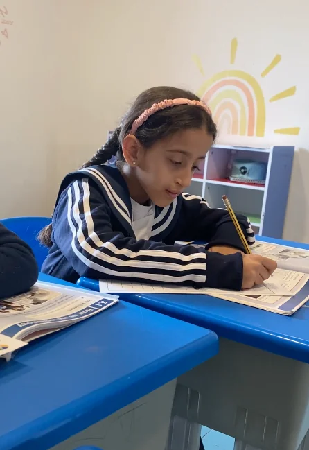 Primary pupil reading and writing at a blue classroom table